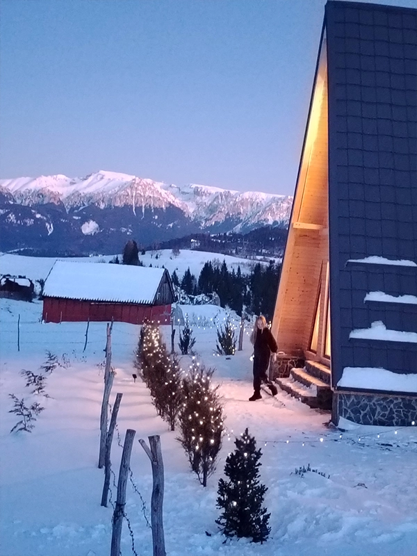 Cabana Alloria la ceas de seară, luminată cald, cu decor de iarnă și vedere spre Munții Bucegi